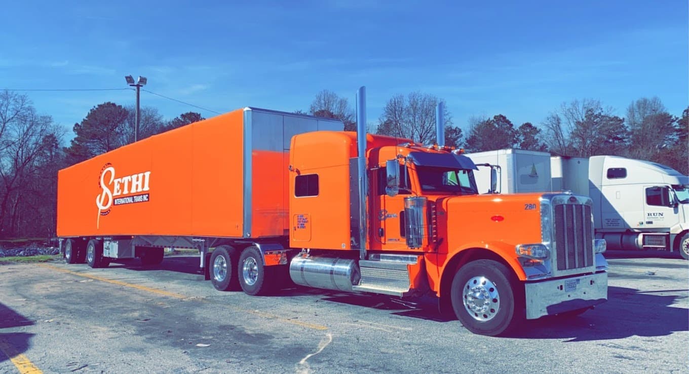 An orange Sethi International Trans truck and trailer parked outdoors